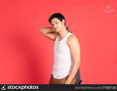 Asian handsome young man with big muscle wearing white vest hand hold take off shirt standing isolated on red background shot in studio.