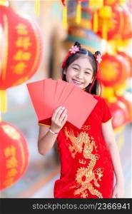 Asian Happy little girl wearing red traditional Chinese cheongsam decoration holding red envelopes in hand and lanterns with the Chinese text Blessings written on it Is a Fortune blessing for Chinese