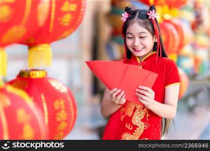 Asian Happy little girl wearing red traditional Chinese cheongsam decoration holding red envelopes in hand and lanterns with the Chinese text Blessings written on it Is a Fortune blessing for Chinese 