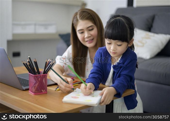 Asian Happy mom and daughter are using laptop for studying online via internet at home. E-learning Concept during quarantine time.