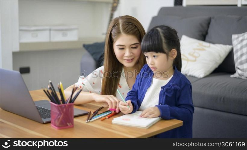 Asian Happy mom and daughter are using laptop for studying online via internet at home. E-learning Concept during quarantine time.