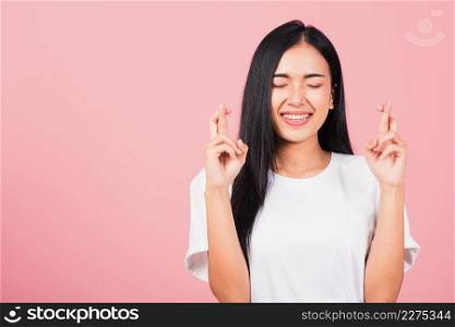 Asian happy portrait beautiful cute young woman smile have superstition her holding fingers crossed for good luck gesture studio shot isolated on pink background, Thai female with copy space