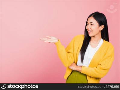Asian happy portrait beautiful cute young woman smile standing presenting product holding something on palm away side, studio shot isolated on pink background with copy space, female show hand gesture