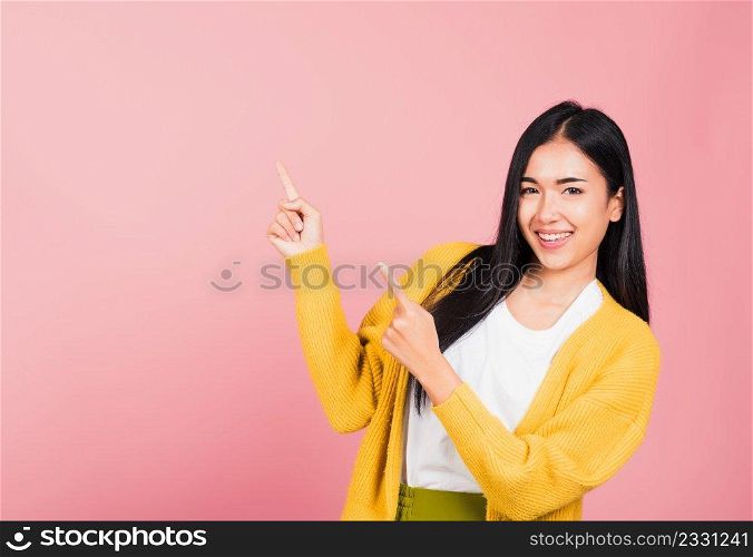 Asian happy portrait beautiful cute young woman standing makes gesture two fingers point upwards above presenting product something, studio shot isolated on pink background with copy space