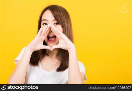 Asian happy portrait beautiful cute young woman teen standing big shout out with hands next mouth giving excited positive looking to camera isolated, studio shot on yellow background with copy space