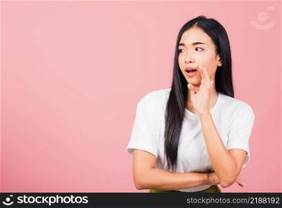 Asian happy portrait beautiful cute young woman teen standing hand on mouth talking whisper secret rumor studio shot isolated on pink background, Thai female looking to side away with copy space