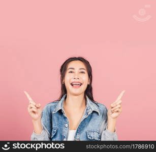 Asian happy portrait beautiful cute young woman wear denim standing makes gesture two fingers point upwards above presenting product something, studio shot isolated on pink background with copy space