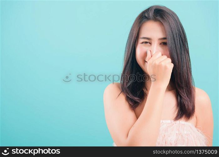 Asian happy portrait beautiful young woman standing smile her very bad smell use hand covers her nose on blue background with copy space for text