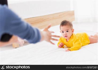Asian happy young mother have fun learn walking crawling his daughter baby indoors bedroom at home. The mom playing with her little baby to crawl, two family