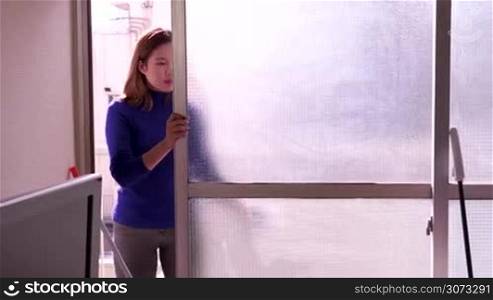 Asian housemaid cleaning hotel room, young woman job, people working. Chinese girl at work as maid doing chores, profession, occupation. Housekeeper wiping window glass with detergent at home