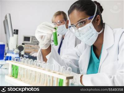 Asian Indian female medical or scientific researcher or doctor looking at a test tube of green solution in a laboratory with her caucasian colleague