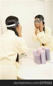 Asian/Indian young woman looking in mirror adjusting eye mask.