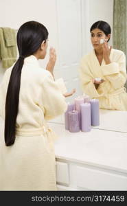 Asian/Indian young woman looking in mirror applying facial scrub.