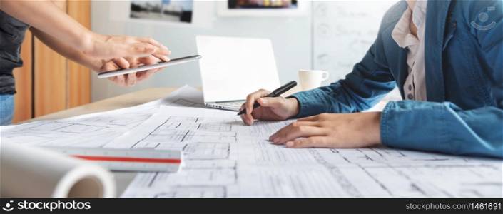 Asian Interior Designer and partner brainstorm and design in building Architecture project. Architect team consult and work for construction on digital tablet, laptop, paperwork, blueprint at office