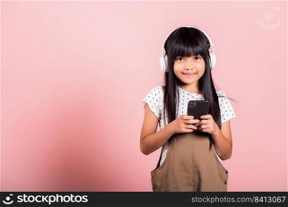 Asian kid 10 years enjoying listening music from mobile phone wear wireless headset at studio shot isolated on pink background, Happy child girl lifestyle use smartphone listen music with headphones