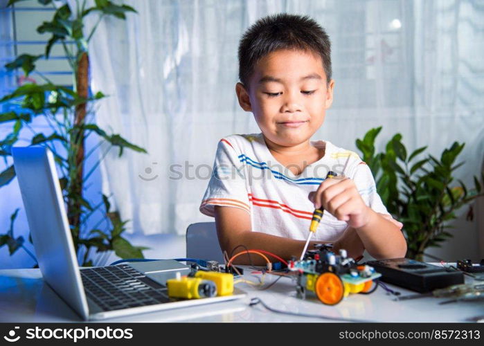 Asian kid boy assembling the Arduino robot car homework project at home, Little child tighten the nut with a screwdriver to assemble car toy, creating electronic AI technology workshop school lesson