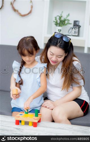 Asian kid girl and mother playing toy block; together with cheerful and happy in living room, activity in family.