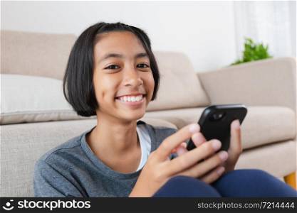 Asian kid girl are watching video that are joking on online media. The little girl using the smartphone to watch video for entertainment on sofa at home