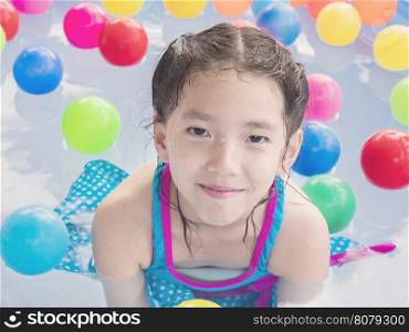 Asian kid is playing in a kid water pool with colorful balls