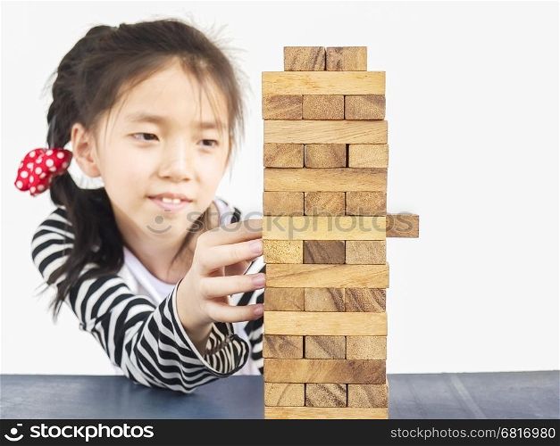 Asian kid is playing jenga, a wood blocks tower game for practicing physical and mental skill