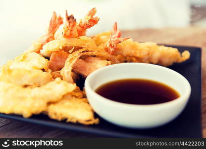 asian kitchen, food, culinary and cooking concept - close up of deep-fried tempura shrimps with soy sauce on table at restaurant