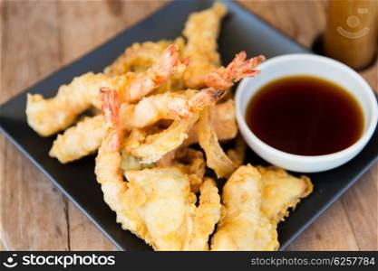 asian kitchen, food, culinary and cooking concept - close up of deep-fried tempura shrimps with soy sauce on table at restaurant