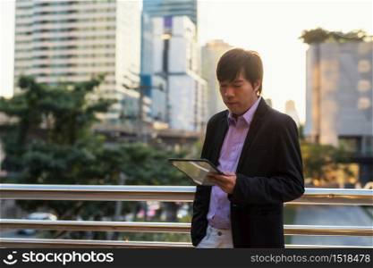Asian Korean CEO businessman, 40s years old or middle age man, chat, check business project plan by tablet outside office building during sunset. Work from corporate application in modern city.