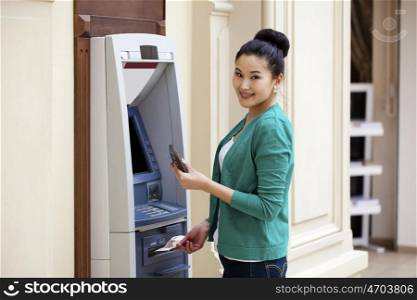 Asian lady using an automated teller machine . Woman withdrawing money or checking account balance