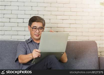 Asian lifestyle senior man with eyeglasses reading news on laptop, Old businessman having video call on laptop computer at home office talk using modern technologies and wireless connection