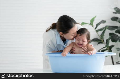 Asian little baby crying with screaming face sitting in bathtub with young mother is kissing comforting her child while mom bathing her cute daughter at home. Baby bathing concept. White background