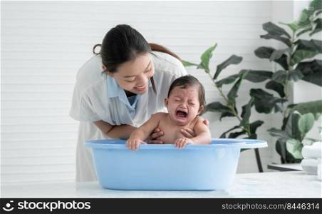 Asian little baby crying with screaming face sitting in bathtub with young mother is comforting her child while mom bathing her cute daughter at home. Baby bathing concept. White background