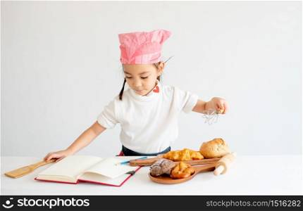 Asian little chef girl prepare and record her recipes about bread and cake cooking on notebook with white background.