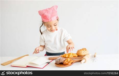 Asian little chef girl test the taste of bread on the table by pick some piece and eat with white background.