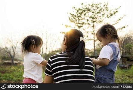 Asian little child girl drink water from bottle after tired of playing in the garden with mother and sister, looking sunset in evening.
