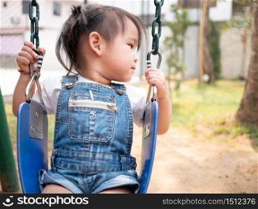 Asian little child is sitting on a swing happily in the playground. Playing is learning for children. Black-white picture.