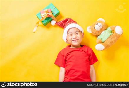 Asian little cute child boy smile, Top view of a kid dressed in red Santa Claus hat the concept of holiday Christmas Xmas day or Happy new year, isolated lying on yellow background