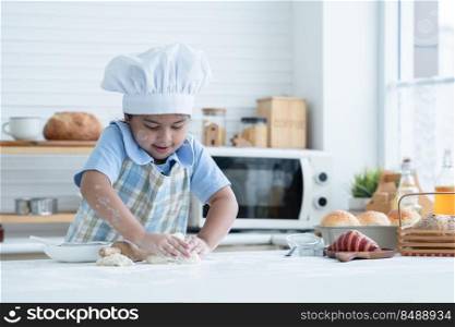 Asian little cute kid girl wear chef hat and apron with flour mess up on face and arms kneading dough bread by her hands in kitchen at home or cooking class at school. Child education concept
