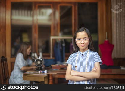 asian little girl dressmaker keeping arms crossed and looking at camera with smile while standing in workshop. asian little girl dressmaker