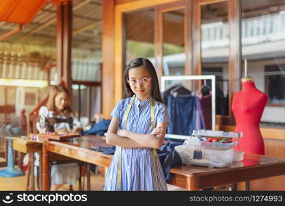 asian little girl dressmaker keeping arms crossed and looking at camera with smile while standing in workshop. asian little girl dressmaker