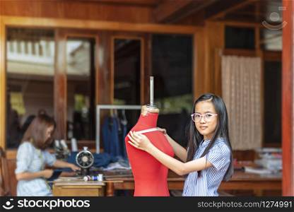 asian little girl dressmaker measuring the dummy and looking at camera with smile while standing in workshop. asian little girl dressmaker