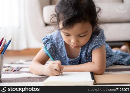 Asian little girl is drawing while lying on the carpet in the living room at her home