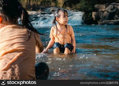 Asian little girl playing in the forest stream with her sister. Active recreation with children on river in summer.