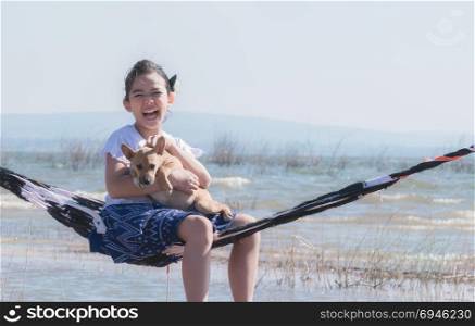 asian little girl playing with her dog on hammock. girl playing with dog on hammock