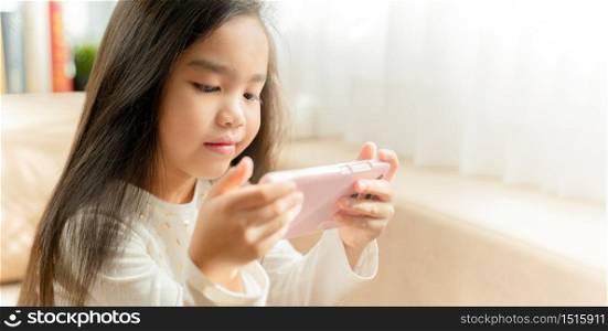 asian little girl playing with smartphone, technology and communication concept - smiling girl texting on smartphone and lying in bed at home
