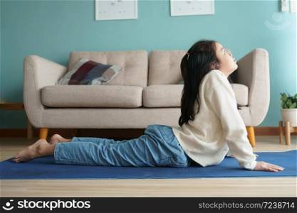 Asian little girl practicing yoga cobra pose on yoga mat in the living at home, Concept of relaxation and meditation