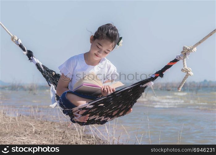 asian little girl reading a book on hammock. girl reading a book