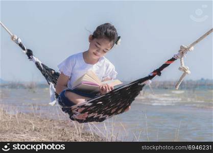 asian little girl reading a book on hammock. girl reading a book