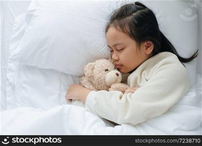 Asian little girl sleeping and hug teddy bear in the bedroom