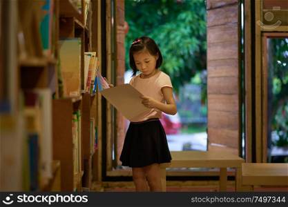 Asian little girl standing and reading book on vintage book library