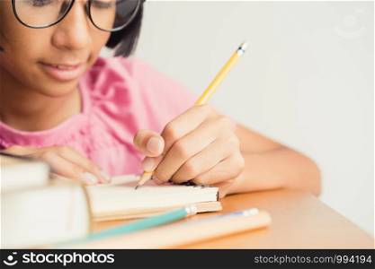 Asian little girl wears glasses while sit writing on desk at her home